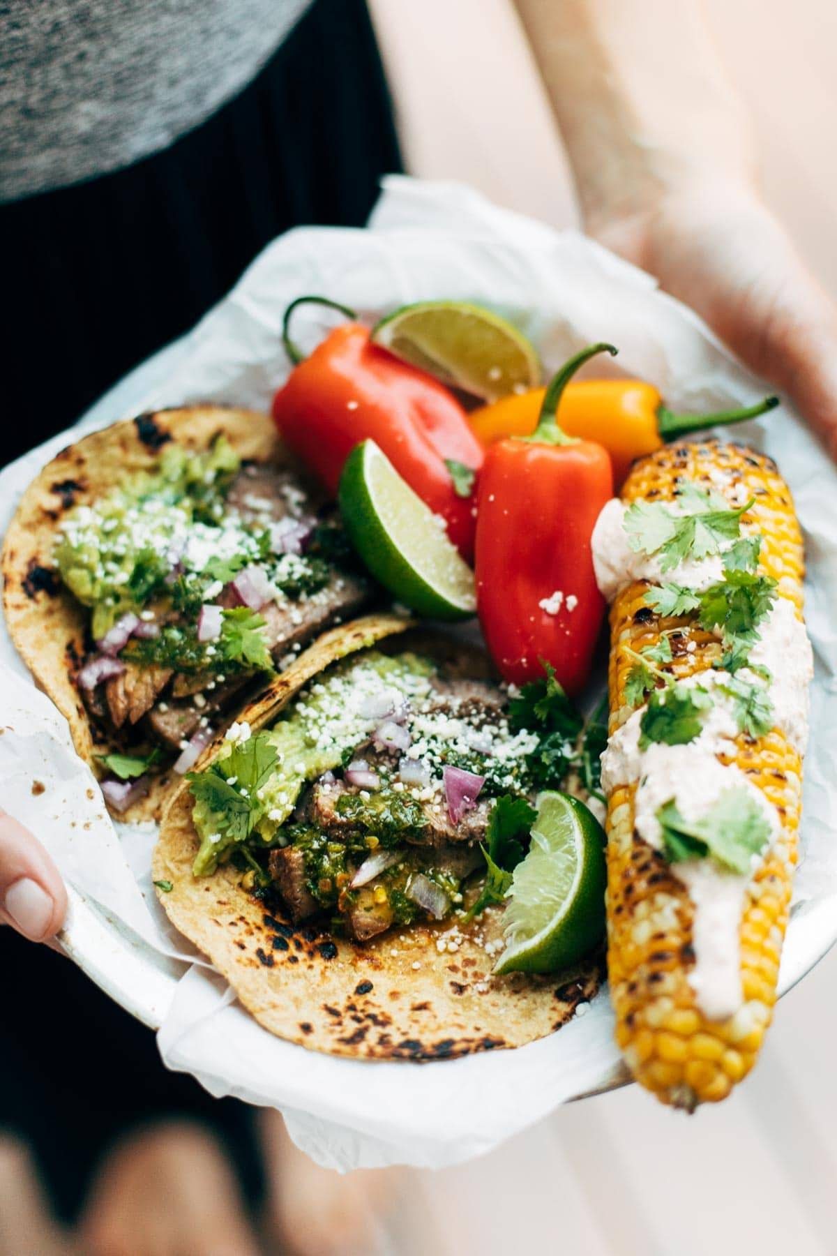 Plate with tacos, grilled corn on the cob, and veggies.